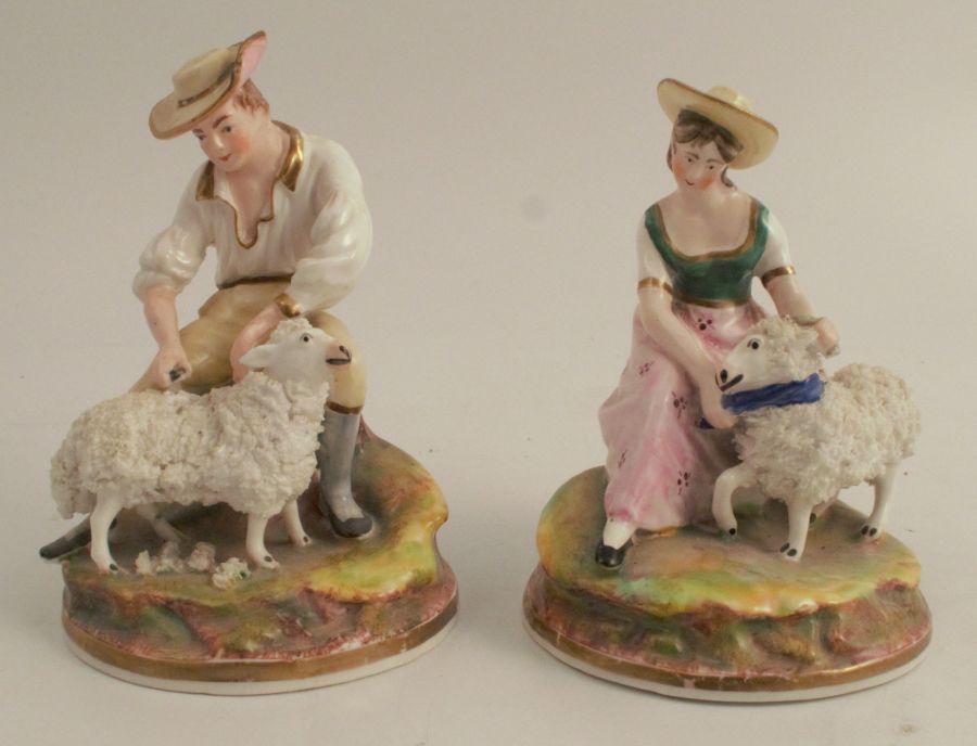 A pair of continental figures, of a man and woman seated with sheep, af, both height 5ins