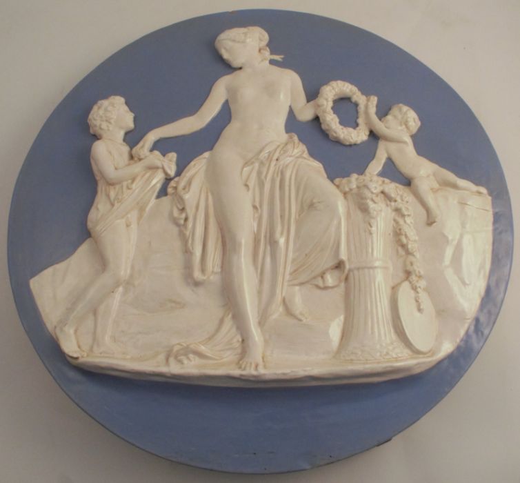 A 19th century English pottery wall plaque, embossed with three Classical figures to a blue