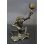 A Cast Bronze Monkey with detachable head, book at feet and holding a stemmed cup aloft, possibly