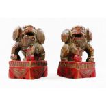 A small pair of Chinese carved wooden temple dogs of foo, painted in red and gilt, on square bases,