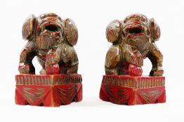 A small pair of Chinese carved wooden temple dogs of foo, painted in red and gilt, on square bases,