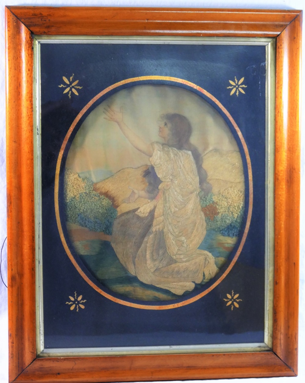 A 19th century oval embroidered silk picture of a young woman kneeling with her arms aloft,