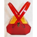 A vintage Lucite handbag, with red body and swing handles and square yellow hinged lid,