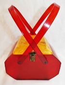 A vintage Lucite handbag, with red body and swing handles and square yellow hinged lid,