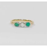 An emerald and diamond three stone ring, the central round brilliant cut diamond approximately 0.