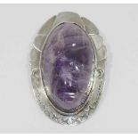 A Mexican carved amethyst oval pendant brooch, the large cabochon carved with a face,