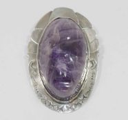A Mexican carved amethyst oval pendant brooch, the large cabochon carved with a face,