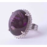 A white metal cluster ring set large Amethyst cabochon surrounded by small diamonds, stamped YK10