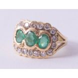 An 18ct emerald and diamond cluster ring, set with three oval cut emeralds, surrounded by eighteen