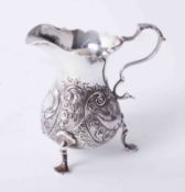 Antique silver cream jug with embossed bird and scroll decoration to body on 3 raised padded feet