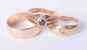 Three 18ct yellow gold rings to include a plain band, gypsy style stone set ring and a garnet set