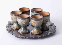 A set of six Doulton art pottery egg cups with silver mounts (some damage).