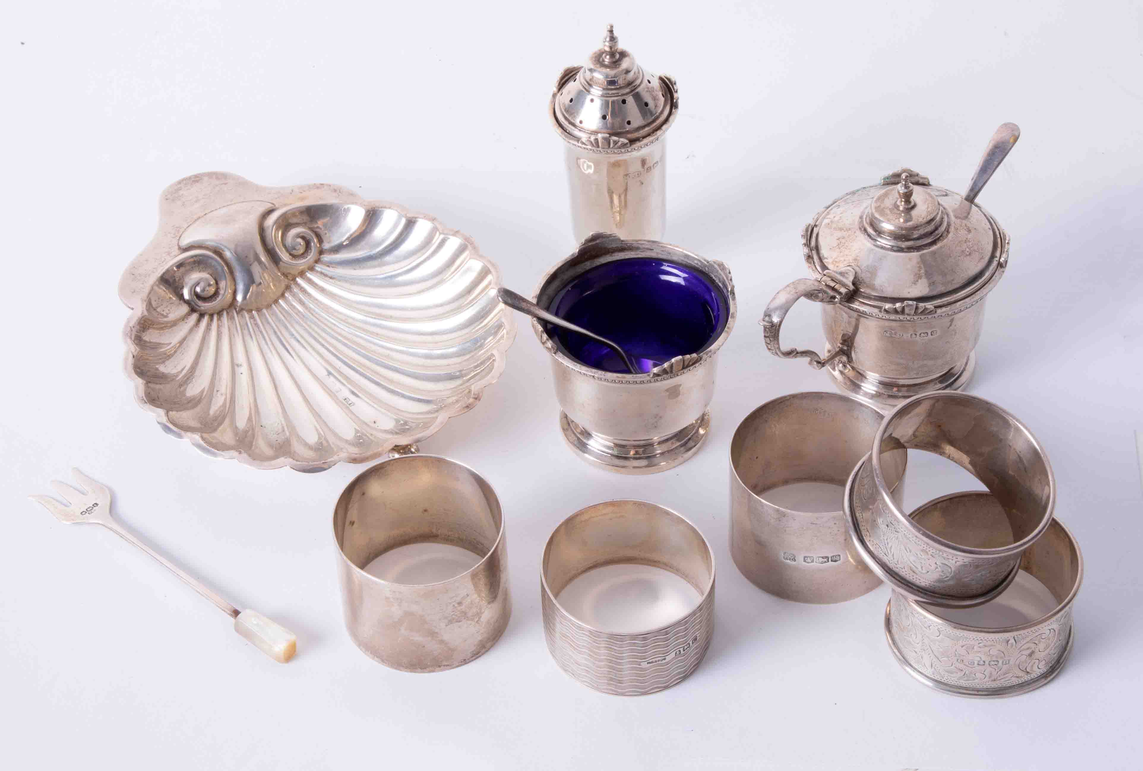 Five assorted silver napkin rings, a silver and scallop shell butter dish and a three piece silver