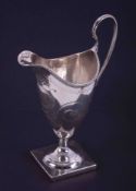 A George III silver helmet shaped cream jug with engraved decoration, monogram within a cartouche,