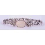 An ornate antique white gold bracelet (no hallmarks) set with an oval cabochon cut white opal