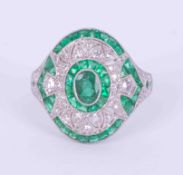 An ornate platinum Art Deco style ring set centrally with an oval cut emerald, 0.25 carats