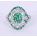 An ornate platinum Art Deco style ring set centrally with an oval cut emerald, 0.25 carats