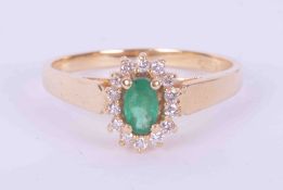 An 18ct yellow gold cluster ring set with an oval cut emerald surrounded by small round brilliant