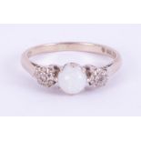 An 18ct white gold three stone ring set with a central cabochon cut white opal, 5.4mm with one round