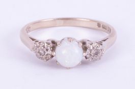 An 18ct white gold three stone ring set with a central cabochon cut white opal, 5.4mm with one round