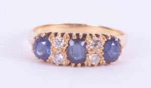 An 18ct yellow gold ring set with three oval cut sapphires, interspaced with four old round cut