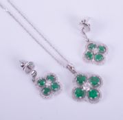 An 18ct white gold flower style pendant set with round cut emeralds and round brilliant cut diamonds
