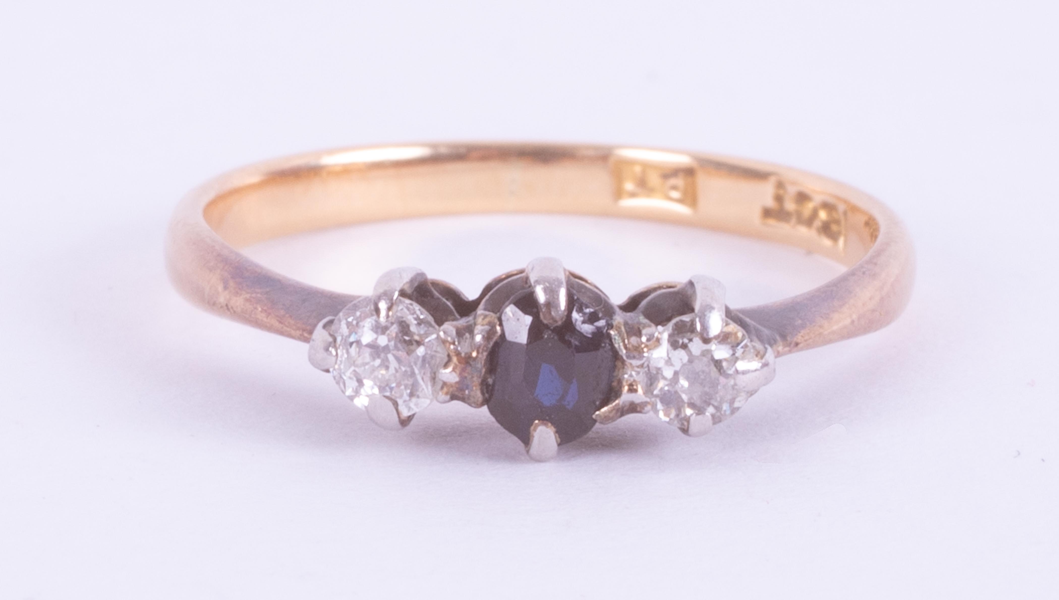 An 18ct yellow & white gold three stone ring set with a central round cut dark blue sapphire with