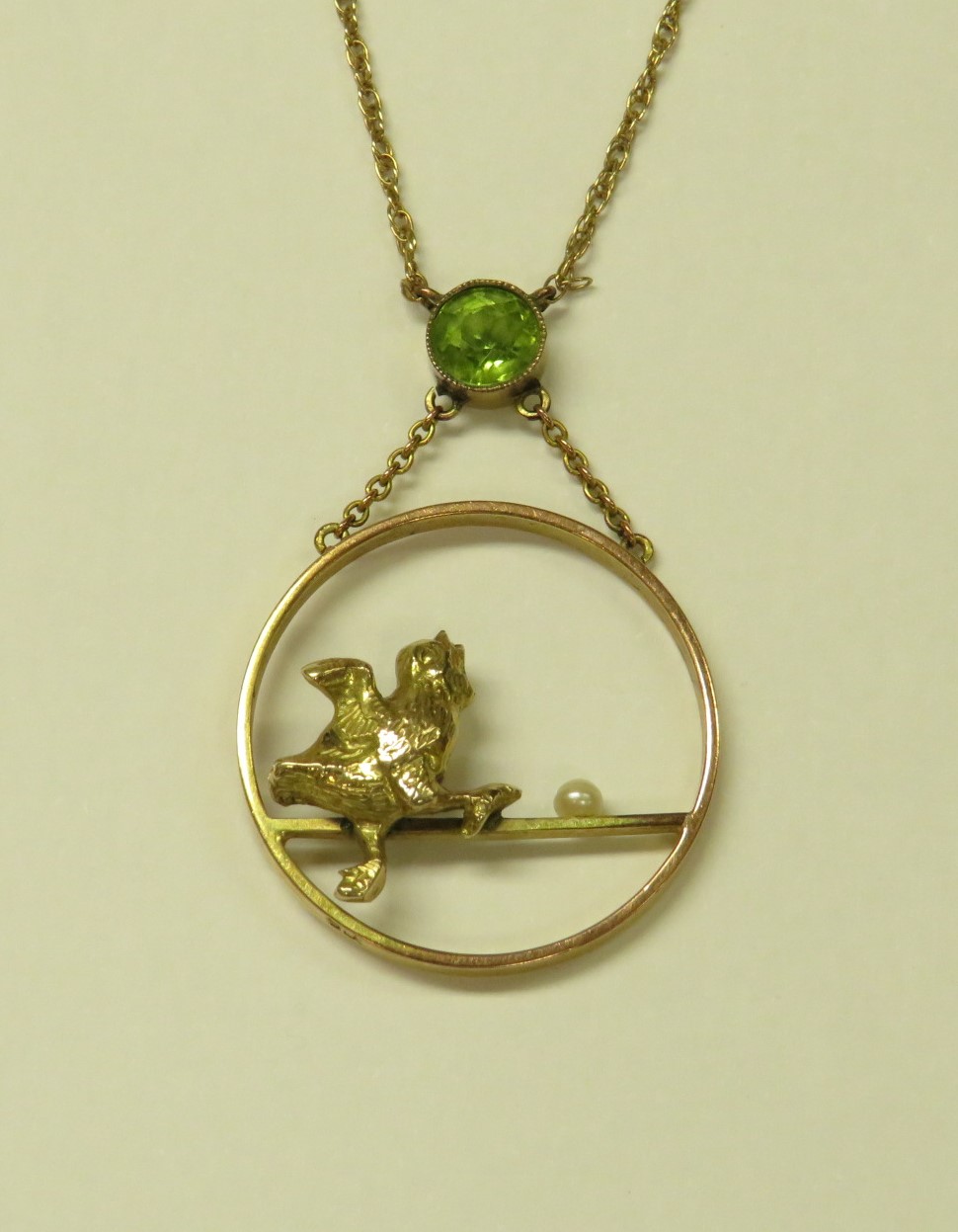 YELLOW METAL HOOP PENDANT SUSPENDED FROM A SET GREEN STONE (PERHAPS PERIDOT), MODELLED WITH A