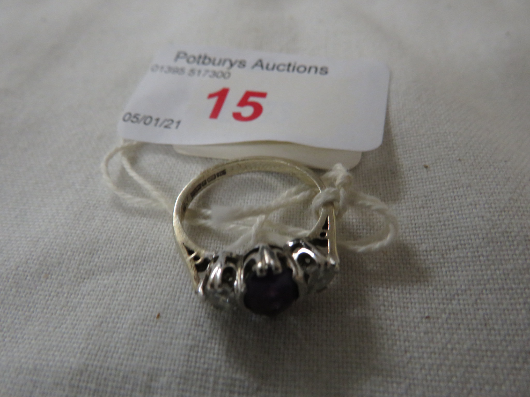 AN IMPORTED SILVER DRESS RING SET CENTRALLY WITH AN OVAL AMETHYST (6MM X 5MM) BETWEEN TWO WHITE FAUX