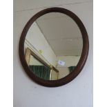 AN OVAL MIRROR IN A MAHOGANY VENEER FRAME.