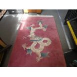 Chinese pink ground woollen carpet decorated with a dragon and a black floral decorated example