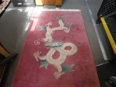 Chinese pink ground woollen carpet decorated with a dragon and a black floral decorated example