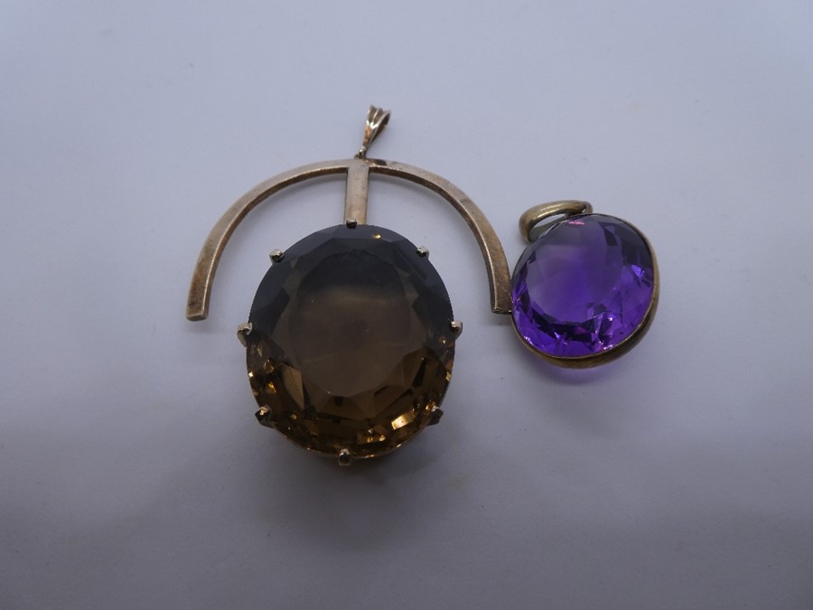 Large yellow metal pendant set with an oval smoky topaz and an amethyst example