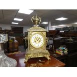 An early 20th century ornate brass chiming mantel clock with urn surmount and scroll feet