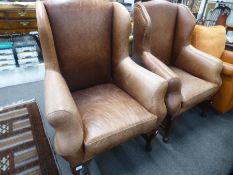 A pair of modern brown leather wing arm chairs on hoof feet