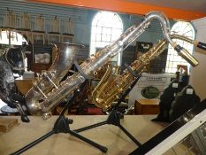 Two Saxaphones on stands one is a tennor by Racso and the other is an Alto both with mouth pieces
