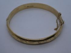 9ct yellow gold bangle with safety chain, dents to top with etched floral decoration, marked 375, 10