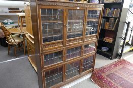 A slimline oak leaded glass sectional book case having carved decoration, 128cm