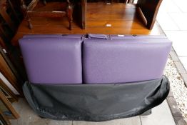 A heavy wooden framed massage bed with purple cushion top, in a black zip up bag