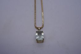 Yellow metal box chain hung with a 9ct yellow gold pendant, with large pale blue stone,