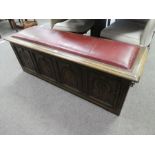 A reproduction oak coffer having carved panelled front with padded lid, 139cm