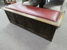 A reproduction oak coffer having carved panelled front with padded lid, 139cm