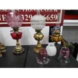 A Victorian brass oil lamp having cranberry font and shade, two other lamps and three shades.