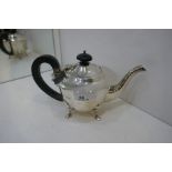 A silver smaller teapot with pretty scalloped edge lid and ebonised wood handle and knop. On four fe