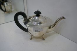 A silver smaller teapot with pretty scalloped edge lid and ebonised wood handle and knop. On four fe