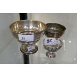 A silver cup on a raised pedestal foot, also with another weighted cup, and a weighted presentation