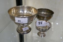 A silver cup on a raised pedestal foot, also with another weighted cup, and a weighted presentation