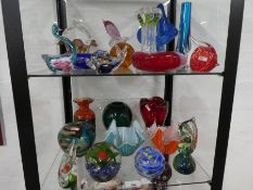 Two shelves of coloured glass items including paper weights and vases.
