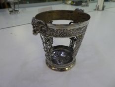 A heavily decorated white metal beaker holder, pierced decoration with two rams heads, dragons desig