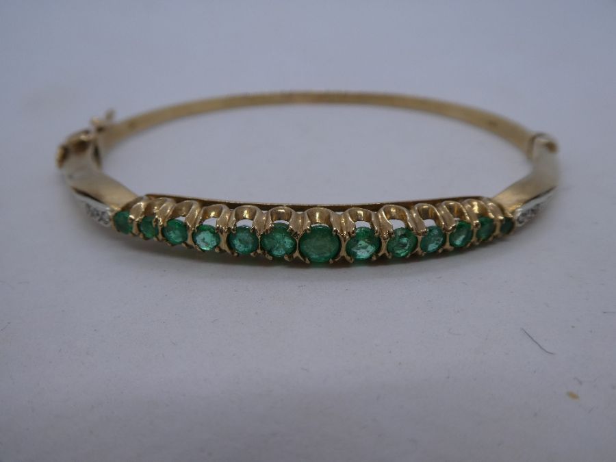 A 20th century 9ct yellow gold emerald and diamond hinged bangle comprising of thirteen round cut em